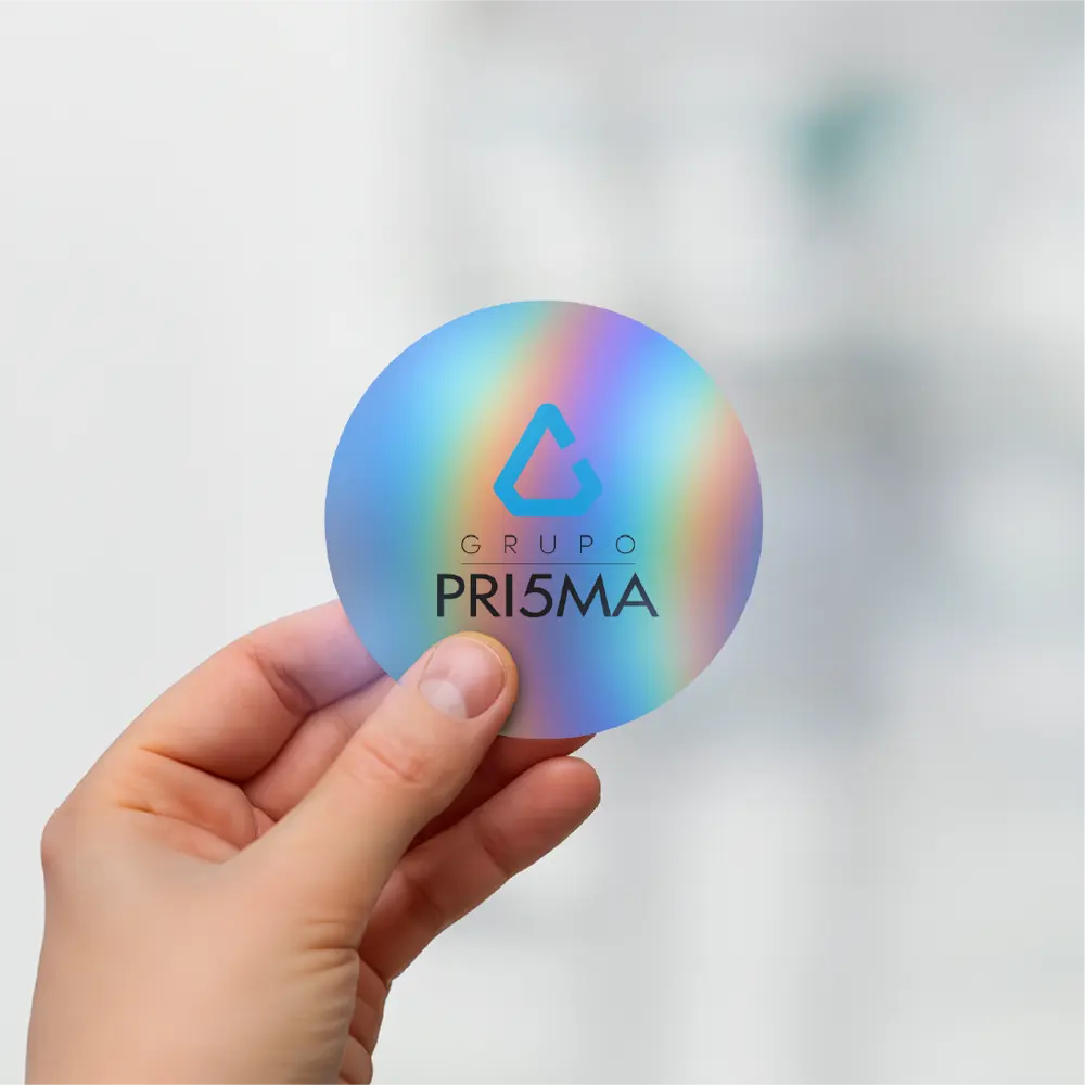 Mano sosteniendo un sticker holográfico con el logo de Grupo PRI5MA